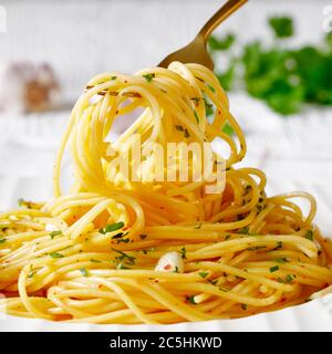 Spaghetti con la colatura di alici, Spaghetti con salsa di acciughe, pepe pimento, aglio e prezzemolo su un piatto bianco e su una forchetta dorata, paesaggio Foto Stock