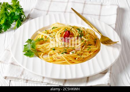 Spaghetti con la colatura di alici, Spaghetti con salsa di acciughe, pepe pimento, aglio e prezzemolo su un piatto bianco con forchetta dorata, paesaggio vi Foto Stock