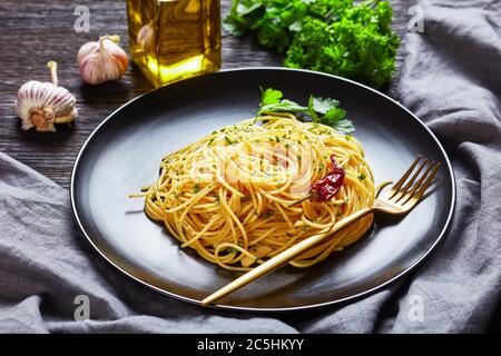 Spaghetti alla colatura di alici, spaghetti con salsa di acciughe, pepe pimento, aglio e prezzemolo su un piatto nero con forchetta dorata al buio Foto Stock