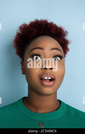 Scioccato, stupito, si chiedeva. Ritratto di una giovane donna afroamericana su sfondo blu dello studio. Bella modello femminile. Concetto di emozioni umane, espressione facciale, vendite, pubblicità. CopySpace. Foto Stock