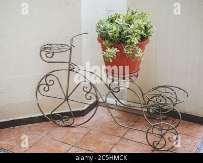 Decorativo in ferro battuto, in forma di bicicletta con pentola, con una pianta si trova sul pavimento sulla piastrella contro la parete bianca Foto Stock