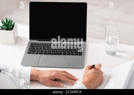 Donna medico mani prendere appunti in notebook, utilizzando il computer portatile, seduto alla scrivania Foto Stock