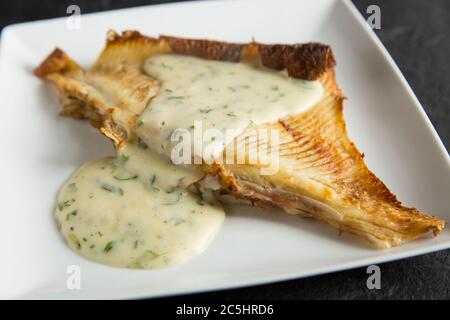 Un'ala di raggio da un raggio di spina, Raja clavata, che è stato arrostito e servito con salsa di prezzemolo. Il raggio è stato catturato da una barca nel Chan inglese Foto Stock