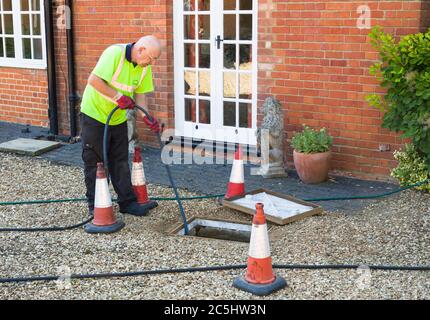 BUCKINGHAM, Regno Unito - 07 agosto 2015. Uomo che eietta scarico di liquame fuori casa, scarico società di pulizia sbloccando tubo di liquame principale, Regno Unito Foto Stock