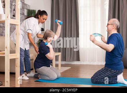 Coppia anziana che fa fisioterapia con il medico. Assistenza domiciliare, fisioterapia, stile di vita sano per anziani, formazione e recupero con fisioterapista professionista Foto Stock