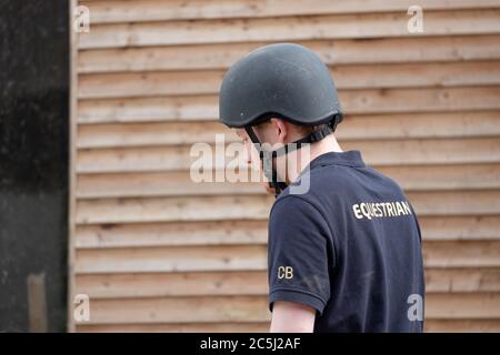 Giovane pilota equestre maschile visto con il casco standard a cavallo durante una giornata di sole. Foto Stock