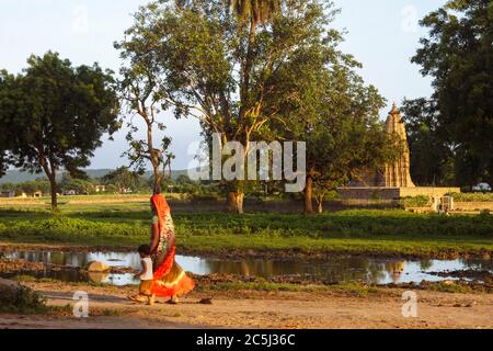 Khajuraho, Madhya Pradesh, India : una donna indiana e un bambino camminano oltre il Tempio Javari, parte del gruppo orientale del sito patrimonio mondiale dell'UNESCO Foto Stock