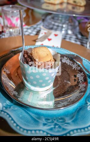 Una colorata festa del tè con cupcake al cioccolato e biscotti con cucchiaino da tè pronti per essere consumati su un piatto blu Foto Stock