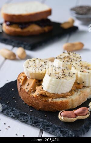 fast food, snack, due panini con marmellata di burro di arachidi e banane su un tavolo di legno bianco Foto Stock