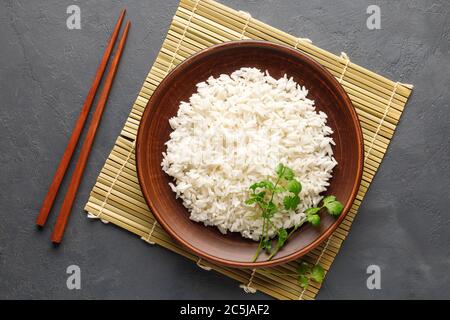 Riso bollito, bastoncini e tovagliolo di bambù su fondo grigio in cemento. Cucina asiatica. Vista dall'alto. Foto Stock