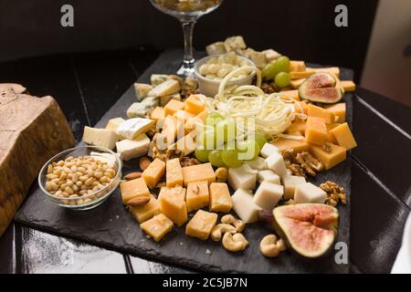 Formaggi assortiti o cheeseboard. Formaggi gourmet con fichi, uva verde e noci su tavola di legno nero. Focus su parmigiano con mandorle al centro di Foto Stock