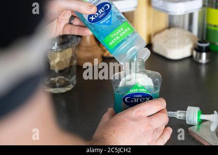 Un uomo che tiene un contenitore della pompa igienizzante per lavaggio a mano con sapone liquido antibatterico Carex (Cussons) e lo riempie con una bottiglia di riempimento Foto Stock