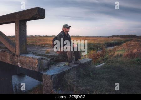 Un uomo con uno zaino seduto su un vecchio ponte di cemento Foto Stock