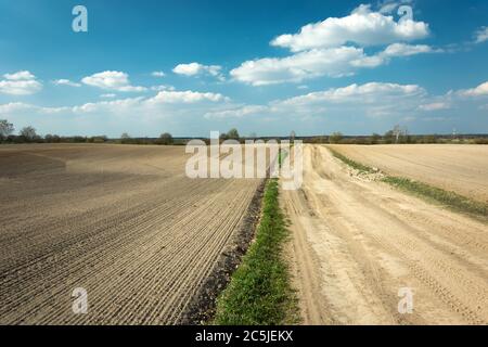 Una strada sabbiosa attraverso i campi arati, giorno di sole primaverile Foto Stock