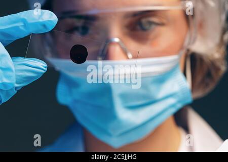 Donna scienziata che guarda il vetrino con il campione di sangue vicino al microscopio in laboratorio Foto Stock