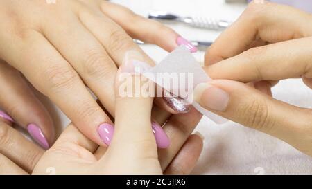 Manicure. Donna che rimuove lo smalto glitterato su un asciugamano bianco. Cura per unghie - rimozione smalto unghie. Il manicure rimuove il lucidante per unghie con un tampone di cotone Foto Stock