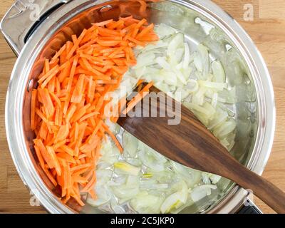 In una padella, affettato cipolle e carote. Friggere gli alimenti. Utensili in metallo con ingredienti, vista dall'alto. Foto Stock