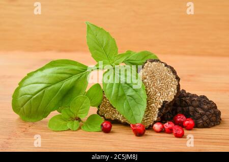 Tartufo nero tagliato a metà su fondo ligneo, con basilico, origano e pepe rosso Foto Stock