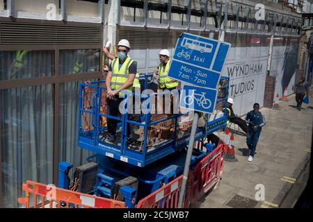 Un operaio che indossa un tabard ad alta visibilità e una copertura facciale, si erge come un punto di osservazione di sicurezza che si affaccia sui pedoni che camminano sotto, durante la costruzione di nuovi appartamenti sulla Walworth Road vicino a Camberwell, il 3 luglio 2020, a Londra, Inghilterra. Foto Stock