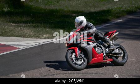 Uomo che corre moto in curva asfaltata con rurale, moto pratica inclinando in una curva veloce in pista Foto Stock