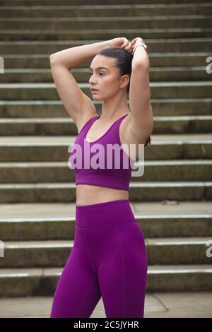 Donna che indossa leggings e reggiseno sportivo con le braccia sollevate vicino alla testa Foto Stock