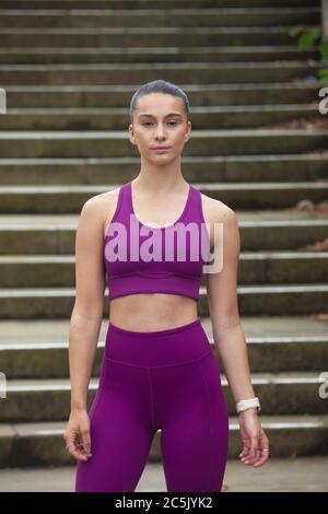 Una giovane donna attraente che indossa abbigliamento sportivo in piedi davanti a una serie di gradini, pronta per l'esercizio. Foto Stock