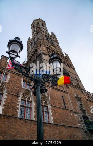 Guardando verso il Campanile di Bruges, il campanile medievale, la città patrimonio mondiale dell'UNESCO, durante l'inverno in un cielo blu sfondo, vecchio palo di lampada di sile Foto Stock