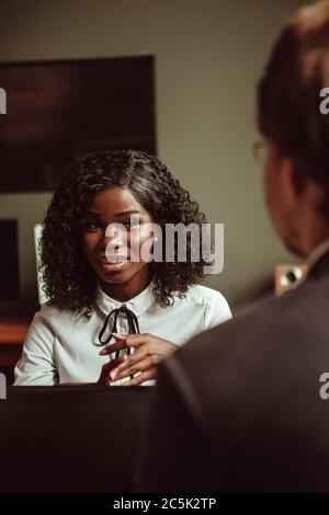 Giovane donna africana in un colloquio o in un incontro d'affari. Fuoco selettivo sul volto sorridente femminile. Ritratto di donna d'affari con pelle scura con Aro Foto Stock