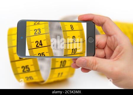 Nastro di misurazione giallo sullo schermo dello smartphone. Misurazione della lunghezza e della circonferenza. Perdere peso e ottenere grasso. Foto Stock