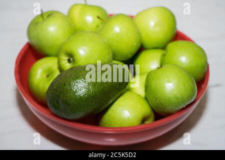 mele verdi e avocado in una tazza rossa sul tavolo Foto Stock
