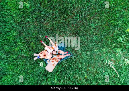 Madre e due figlie hanno un picnic con pizza su un'erba verde, vista aerea dall'alto Foto Stock