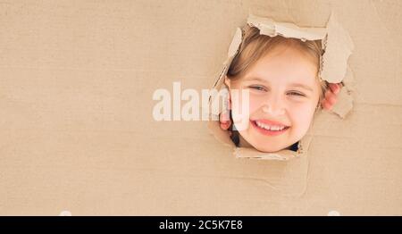 La bambina sorride guardando direttamente dalla scatola di cartone. Foto Stock