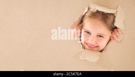 Funnt ragazza piccola che guarda attraverso il foro strappato in scatola di cartone Foto Stock