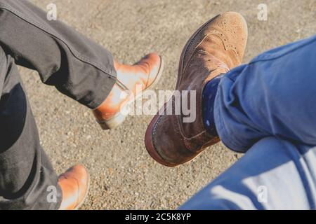 Uomo e donna veduto seduti in un parco. L'uomo sulla destra indossa jeans blu chiaro e scarpe in pelle scamosciata Foto Stock