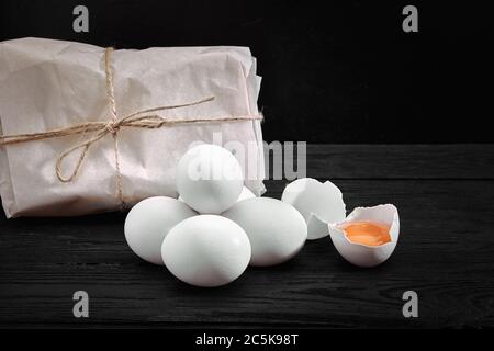 Uova bianche di pollo fresche con fieno su sacco e legno rustico, agricoltura biologica su sfondo nero. Cibo sano e naturale Foto Stock