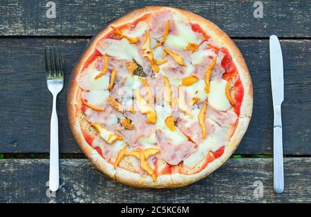 Pizza Chanterelle appena sfornata con forchetta e coltello su vecchio tavolo di quercia grunge Foto Stock