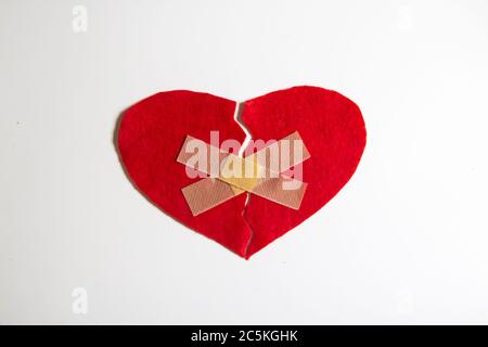 Cuore rotto e incollato insieme con un aiuto-banda. Un cuore dal feltro. Un concetto di amore rotto. Cuore con intonaco isolato su sfondo bianco Foto Stock
