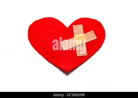 Cuore rotto e incollato insieme con un aiuto-banda. Un cuore dal feltro. Un concetto di amore rotto. Cuore con intonaco isolato su sfondo bianco Foto Stock