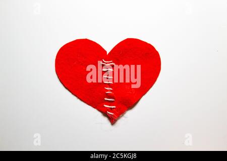 Cucito un cuore rotto con un filo. Cuore rosso fatto di feltro. Concetto di amore rotto. Cuore fisso con filo. Foto Stock