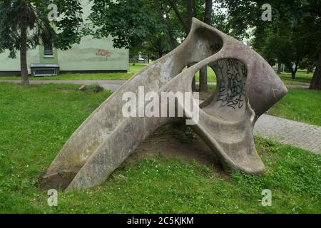 Scivolo in cemento per bambini progettato dallo scultore ceco modernista Eleonora Haragsimová (1965) installato nel cortile del complesso residenziale sperimentale Invalidovna nel quartiere Karlín di Praga, Repubblica Ceca. Lo scivolo ufficialmente conosciuto come il pesce (Prolézačka Ryba) è soprannominato come osso pelvico mammut dalla gente locale. Infatti lo scivolo per bambini è una scultura modernista. Durante il regime comunista in Cecoslovacchia uno dei pochi modi per installare opere d'arte moderniste nelle aree pubbliche era fingere che l'opera d'arte fosse un elemento di un parco giochi. Foto Stock