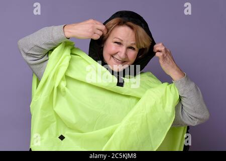 Donna caucasica anziana che indossa un impermeabile verde Foto Stock