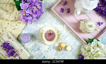 Rilassarsi a casa con tè alla lavanda in stile igge e vassoio, libri antichi e un maglione accogliente su sfondo bianco testurizzato. Vista dall'alto della composizione creativa piatta Foto Stock