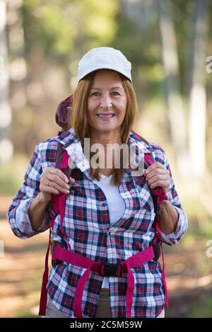 Ritratto attivo attraente donna matura trekking felice e rilassato con zaino nei boschi, sfondo sfocato. Foto Stock