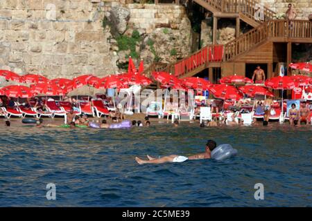 Un uomo galleggia su un materasso ad aria nell'acqua della baia di Antalya adiacente alle antiche mura romane del porto della città vecchia di Kaleici ad Antalya, Turchia. Foto Stock