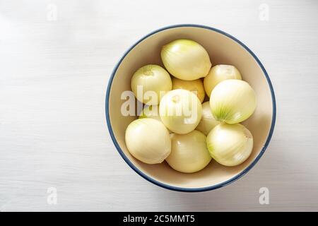 Cipolle biologiche appena sbucciate in una ciotola su un tavolo dipinto di bianco, cucina sana a casa durante la pandemia del coronavirus, spazio di copia, vista ad alto angolo Foto Stock