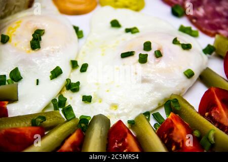 Deliziosa colazione con uova, salumi, cetrioli, pomodori ciliegini, salse e cipolla verde su un piatto bianco. Pasto sano e gustoso per la colazione Foto Stock