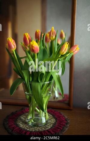 Bouquet di tulipani rosso-giallo in vaso di vetro di fronte a uno specchio, arredamento domestico, vita still, fuoco selettivo Foto Stock