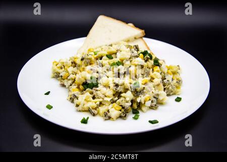 Insalata Ucraina e russa Olivier secondo una nuova ricetta su un piatto bianco. Insalata sana Olivier con carne, mais e fette di pane bianco. DELIC Foto Stock