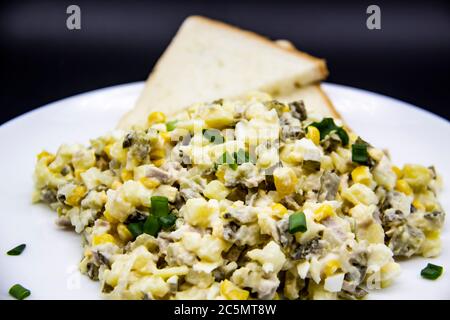 Insalata Ucraina e russa Olivier secondo una nuova ricetta su un piatto bianco. Insalata sana Olivier con carne, mais e fette di pane bianco. DELIC Foto Stock