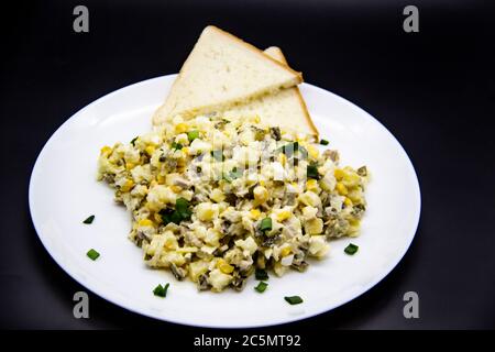 Insalata Ucraina e russa Olivier secondo una nuova ricetta su un piatto bianco. Insalata sana Olivier con carne, mais e fette di pane bianco. DELIC Foto Stock